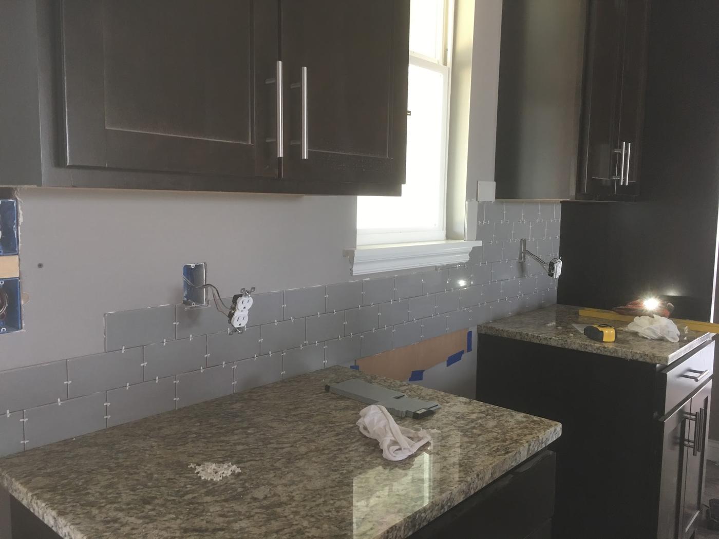 A backsplash being set, spacers still in, run around the outlets and the window.