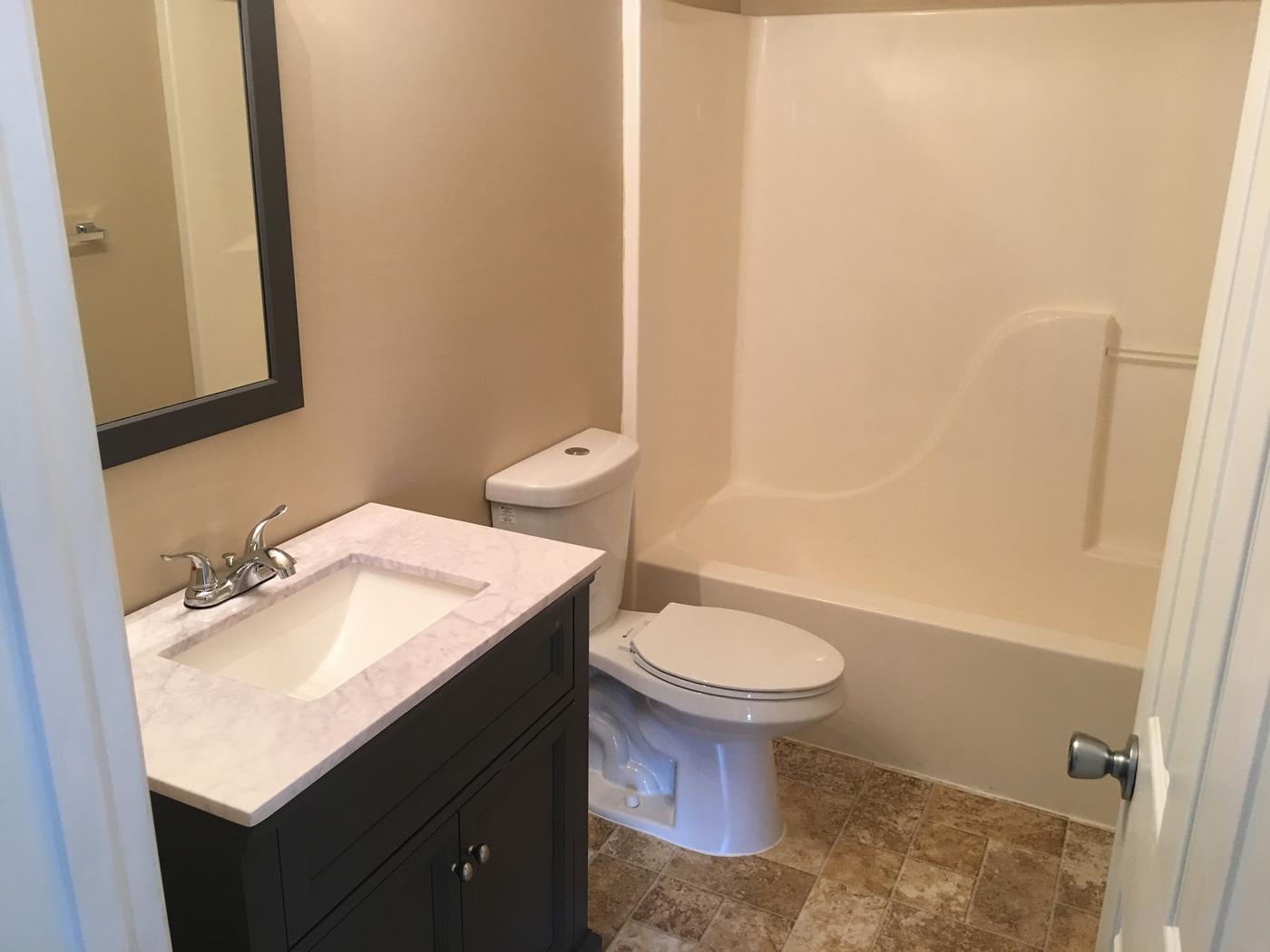 A finished bathroom with a dark vanity, new faucet and tub surround