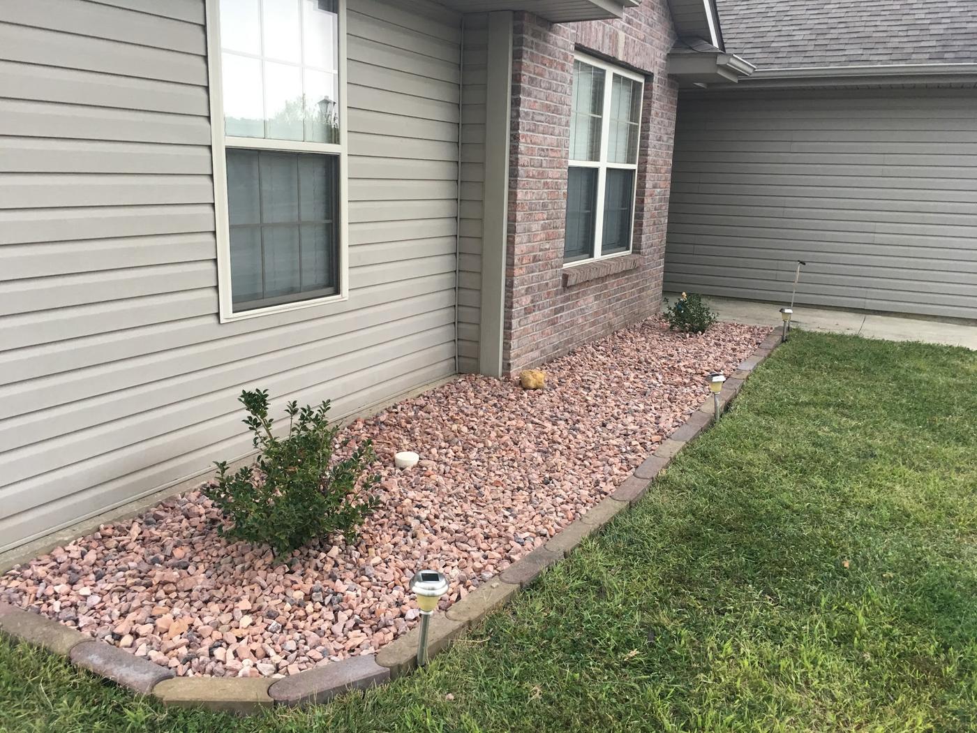 A landscaped bed in pink-toned rock, edged with curved pavers